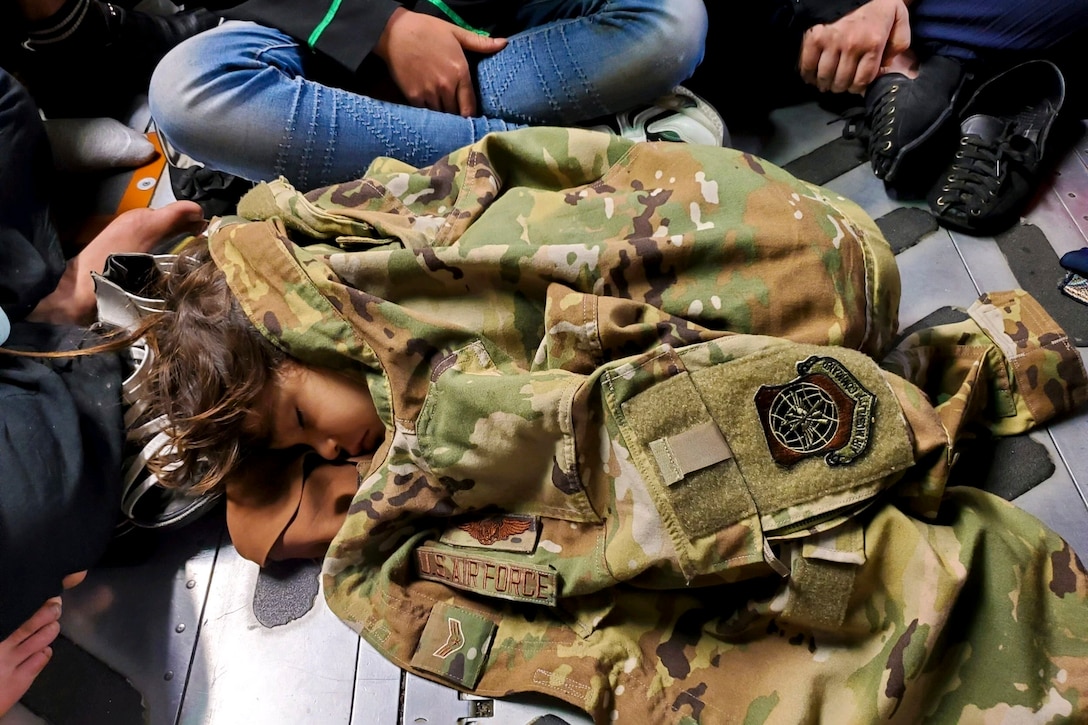 A child sleeps while using a military jacket as a blanket.