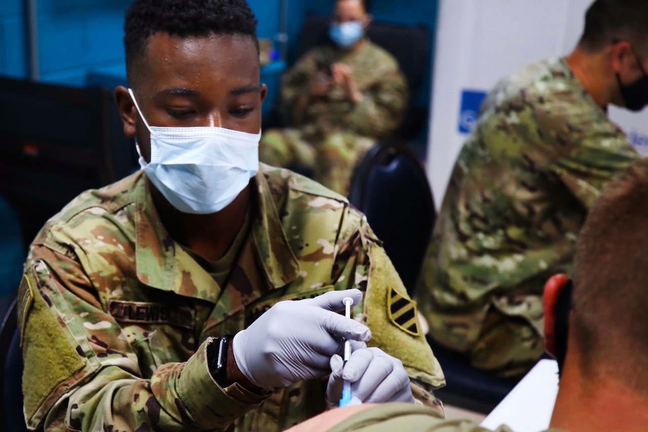 A soldier wearing a face mask and gloves holds a syringe while giving another soldier  a vaccine­­­­.