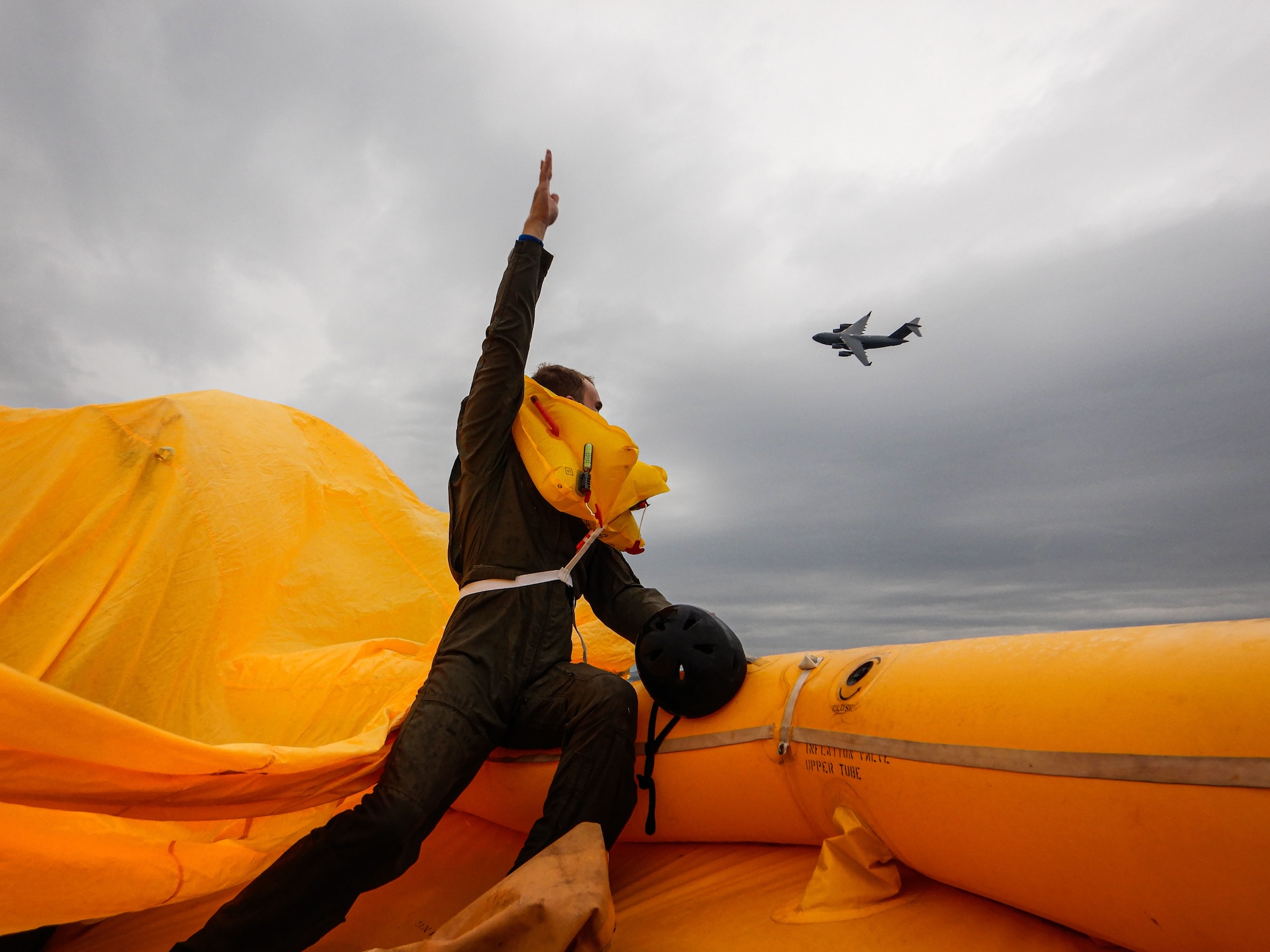 Staff Sgt. Bryan Henry, 436th Operational Support Squadron survival, evasion, resistance and escape flight augmentee, signals at a C-17 Globemaster III near Coast Guard Station Indian River Inlet, Delaware, Aug. 4, 2021. The crew aboard the life raft used several signaling devices like the CSEL radio, sea dye, life raft canopy and flare to vector the C-17 to their location during their exercise. (U.S. Air Force photo by Senior Airman Marco A. Gomez)