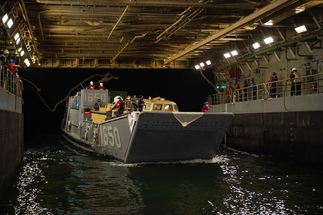 Sailors toss ropes to others riding in a boat in the well deck of a ship.