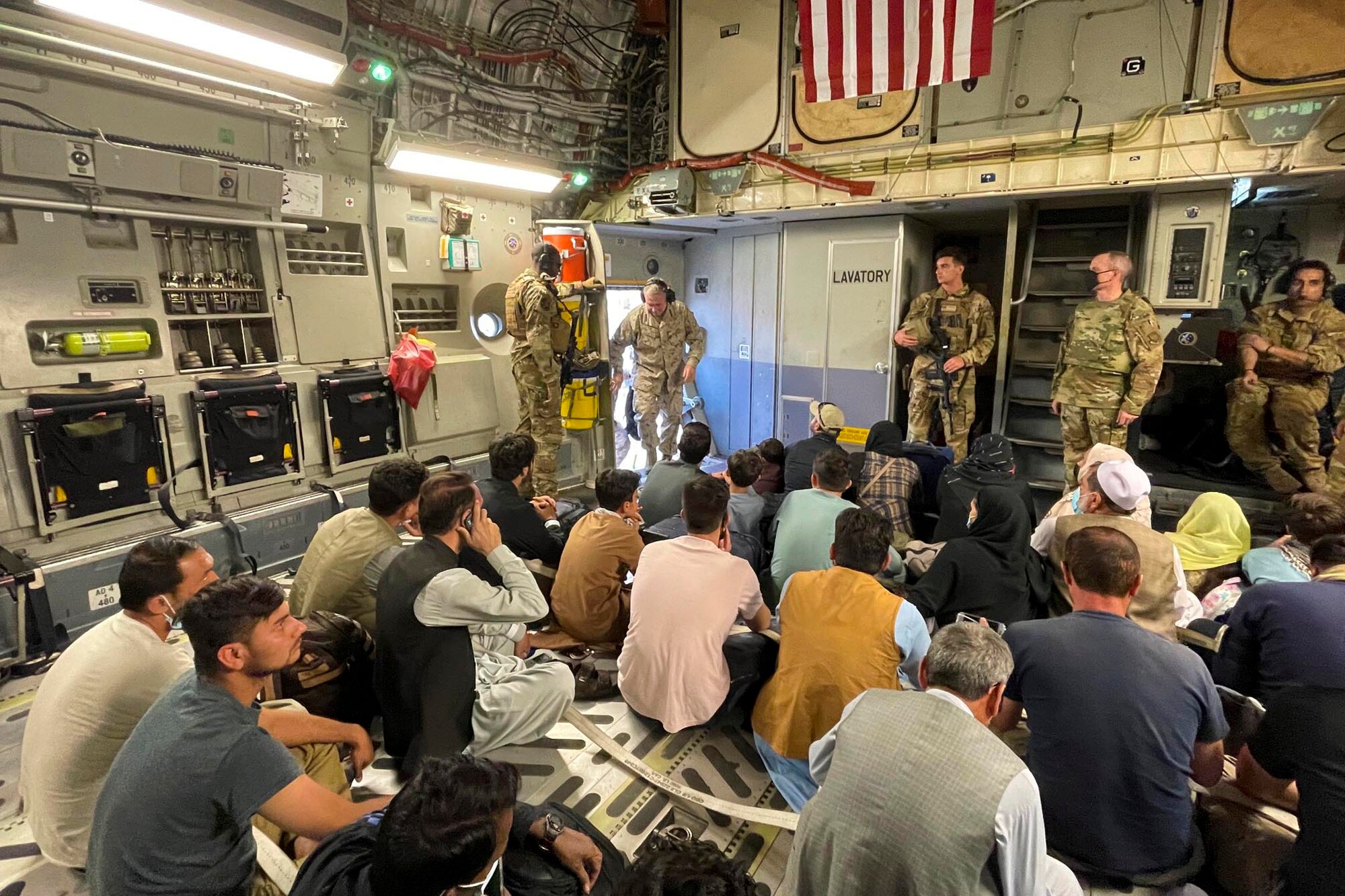 A group of people sit and stand inside of an aircraft.