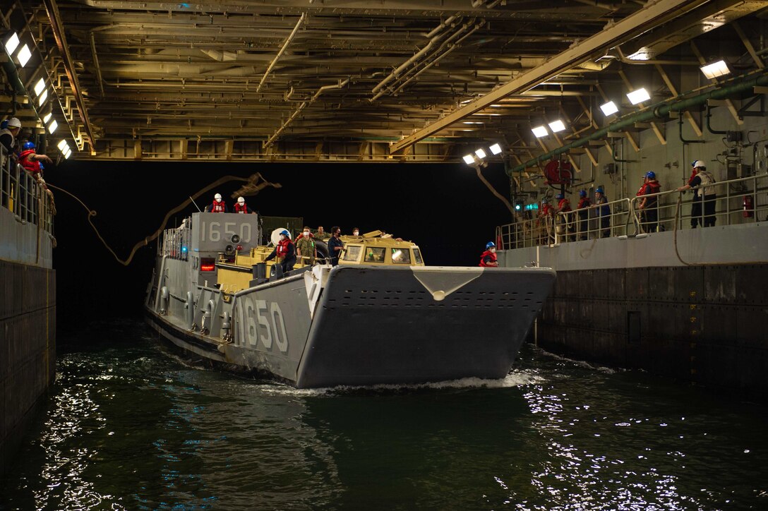 Sailors toss ropes to others riding in a boat in the well deck of a ship.