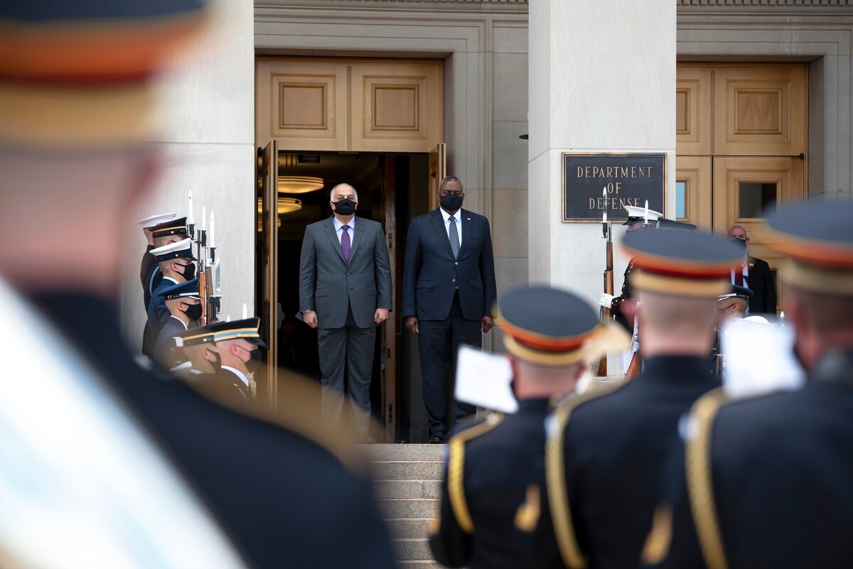 Two men stand atop steps after passing through an honor guard.