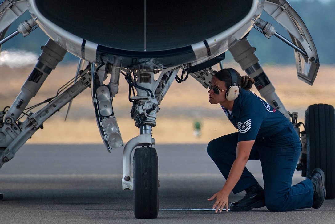 An airman crouches to look underneath an aircraft.