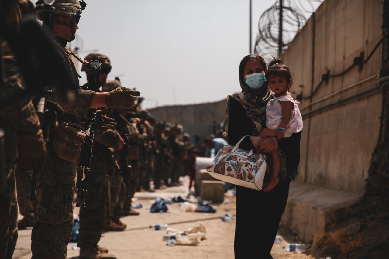 Marines stand in a line facing a woman carrying a child.