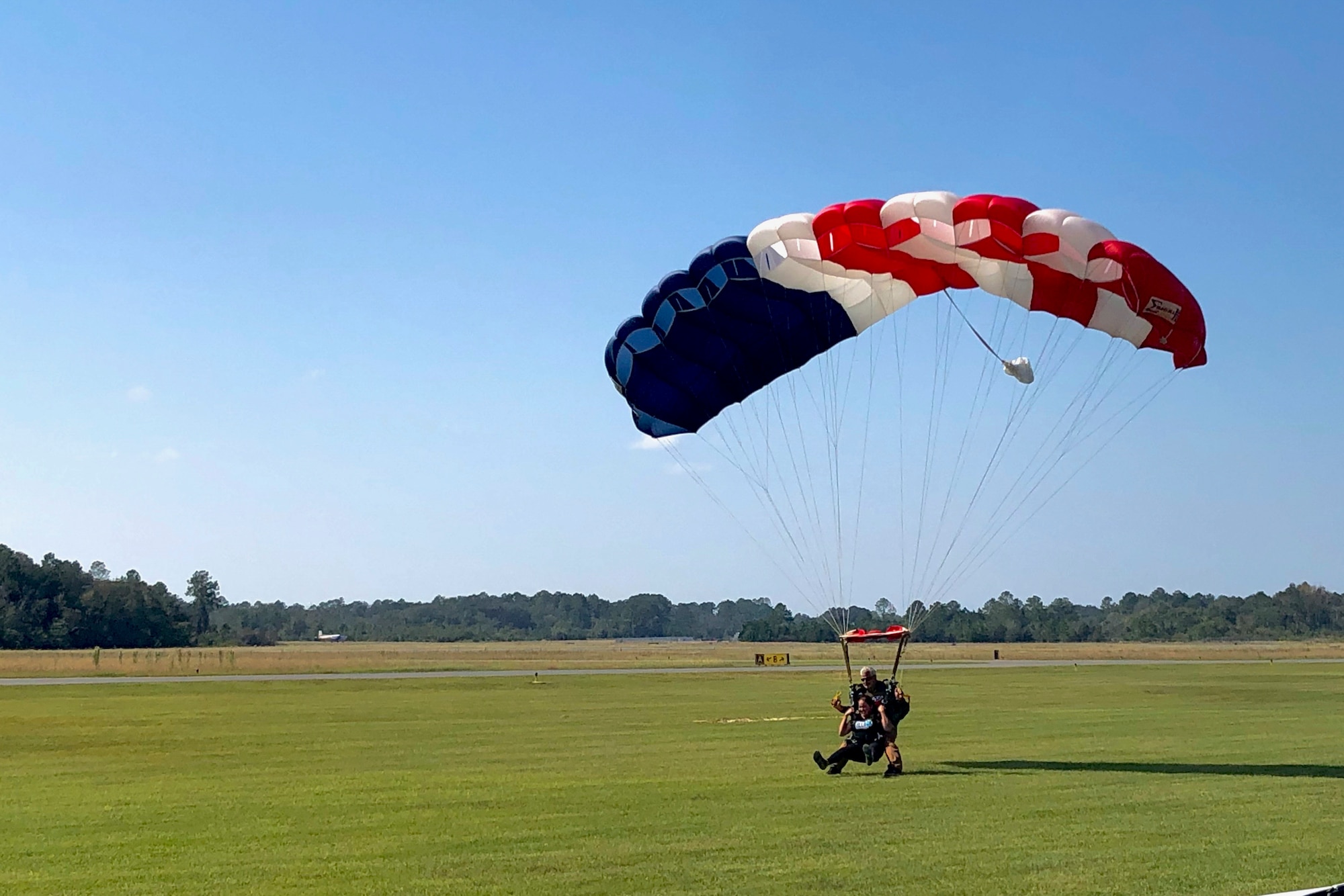 A photo of two people skydiving about to land on the ground.