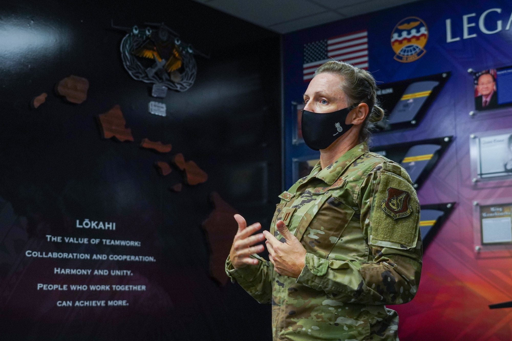 Capt. Carrie Schwartz, 15th Aircraft Maintenance Squadron maintenance operations officer, explains the meaning behind the design of the new Legacy Wall display inside the maintenance building at Joint Base Pearl Harbor-Hickam, Hawaii, August 16, 2021. One side of the wall represents Hawaiian heritage by displaying the islands and the word “Lokahi” meaning the value of teamwork, collaboration, harmony, and unity. (U.S. Air Force photo by Airman 1st Class Makensie Cooper)