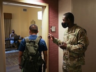 U. S. Army Sgt. 1st Class Demarius Pringle, a forward area support team member from 1st Infantry Division Sustainment Brigade, directs a Navy medical support team member from Navy Medicine Readiness and Training Command Bethesda to Spc. Karen Romo, also assigned to 1st ID SB, for in-processing, Aug. 17, 2021, into a joint operations area during the COVID response operations in Lafayette, Louisiana.