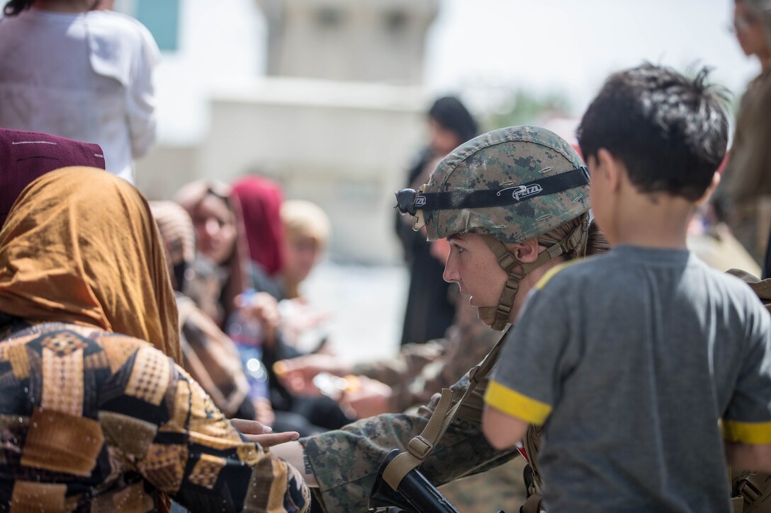 A Marine kneels while talking to a group of people.