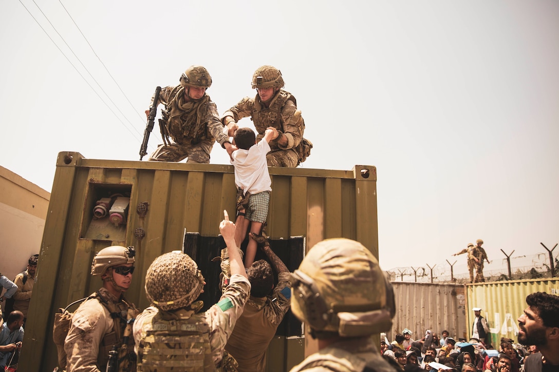 Two service members help life a child onto a truck with help from others on the ground.