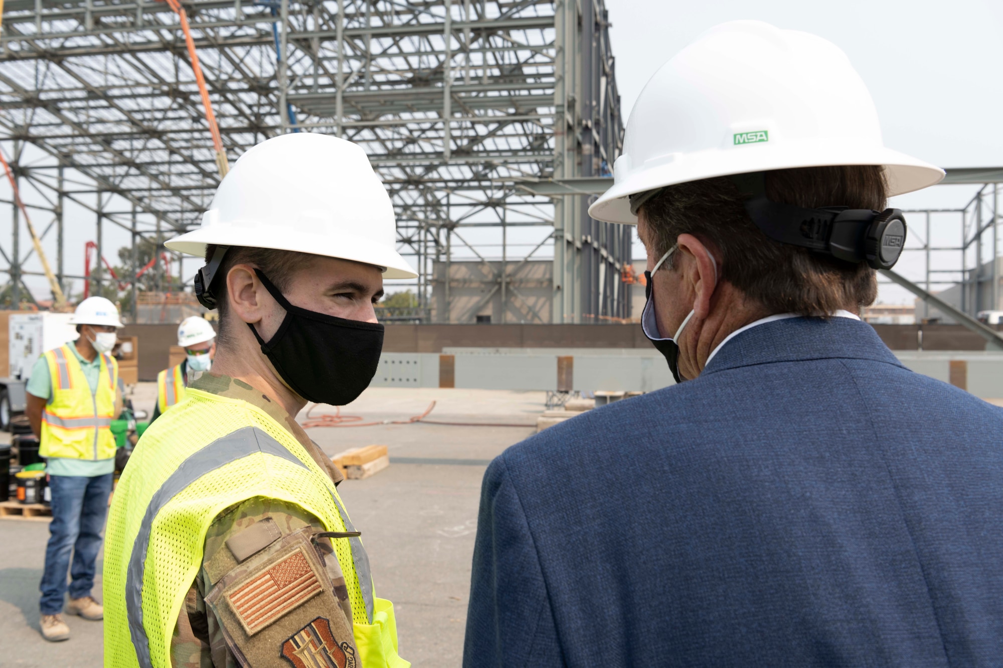 Two men talk in front of a construction site