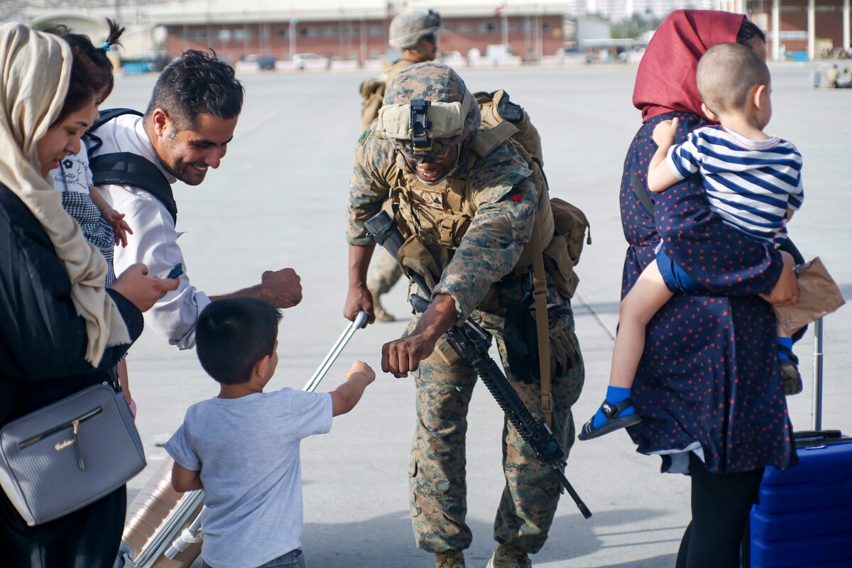 A Marine fist bumps a child as others walk by.