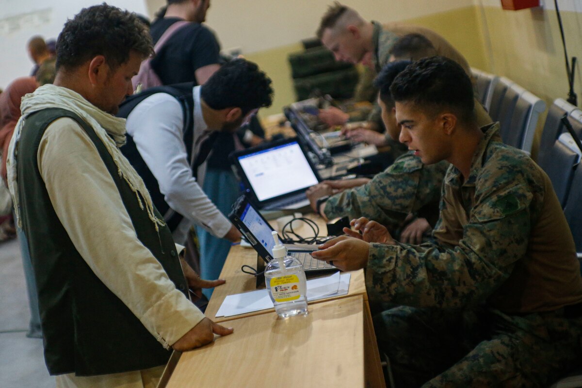 Marines sit at a table as people stand on the other side.