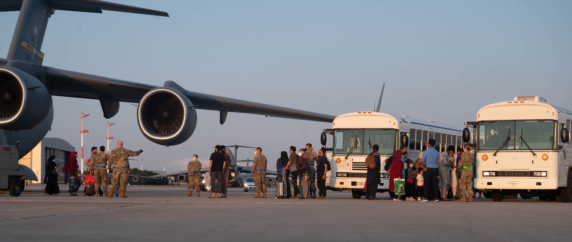 People board buses next to aircraft.