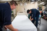 Hospital Corpsman aboard the San Antonio-class amphibious transport dock ship USS Arlington (LPD 24) prepare beds in the medical ward, Aug. 20, 2021.