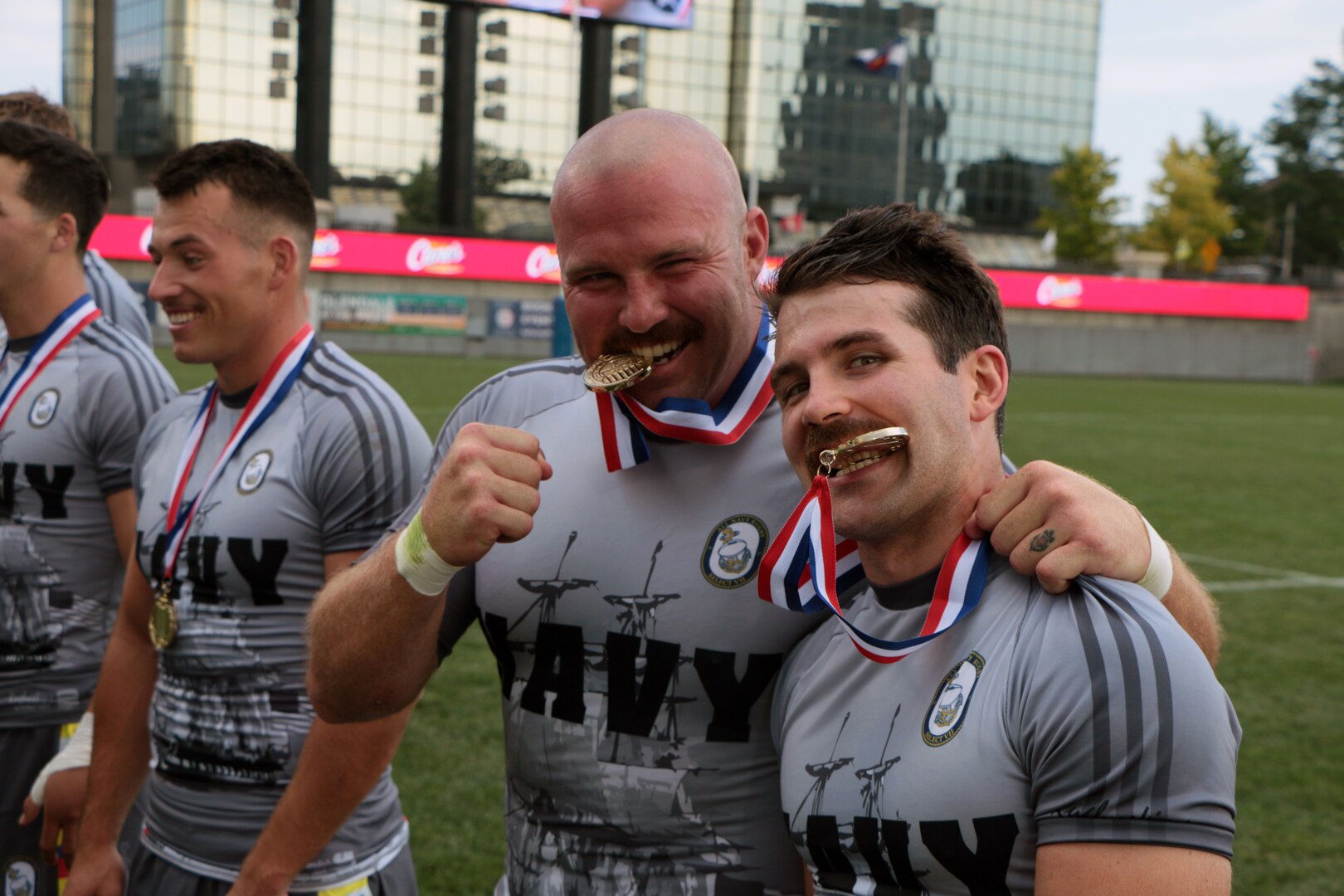 Navy Lieut. Adam D'Amico of Naval Shipyard Portsmouth, Va. (right) and Petty Officer First Class James Irey of Marine Corps Support Facility New Orleans, La. (left) take a bite of their well deserved gold medals after Navy claims victory at the 2021 Armed Forces Rugby Championship held in conjunction with the 2021 Rugbytown 7's Tournament, held from 20-22 August.  Service members from the Navy, Air Force (with Space Force personnel) and Coast Guard battle it out for gold.  (Department of Defense Photo, Released)