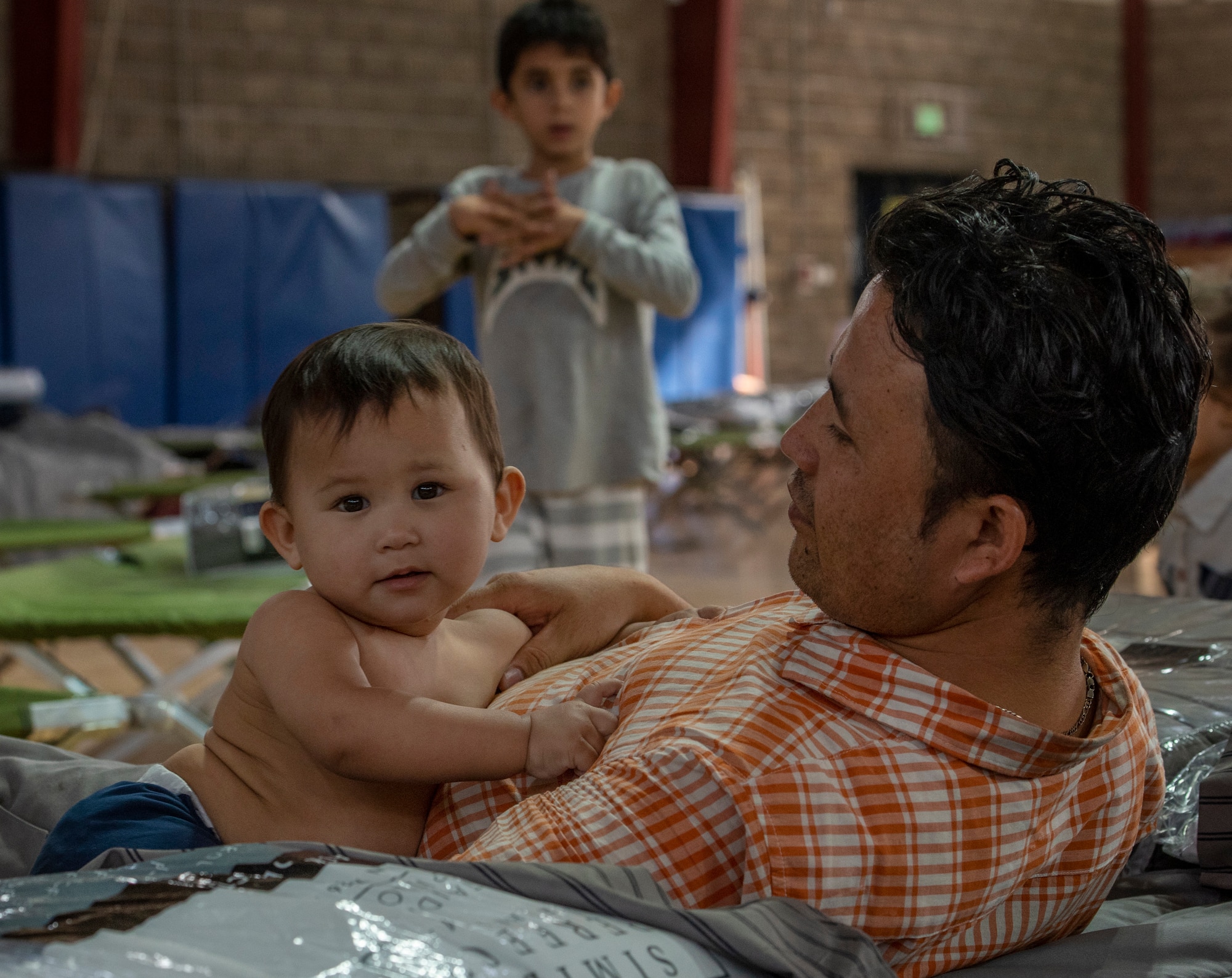 A qualified evacuee lays with his son at a gym in the CENTCOM region, Aug. 20, 2021.