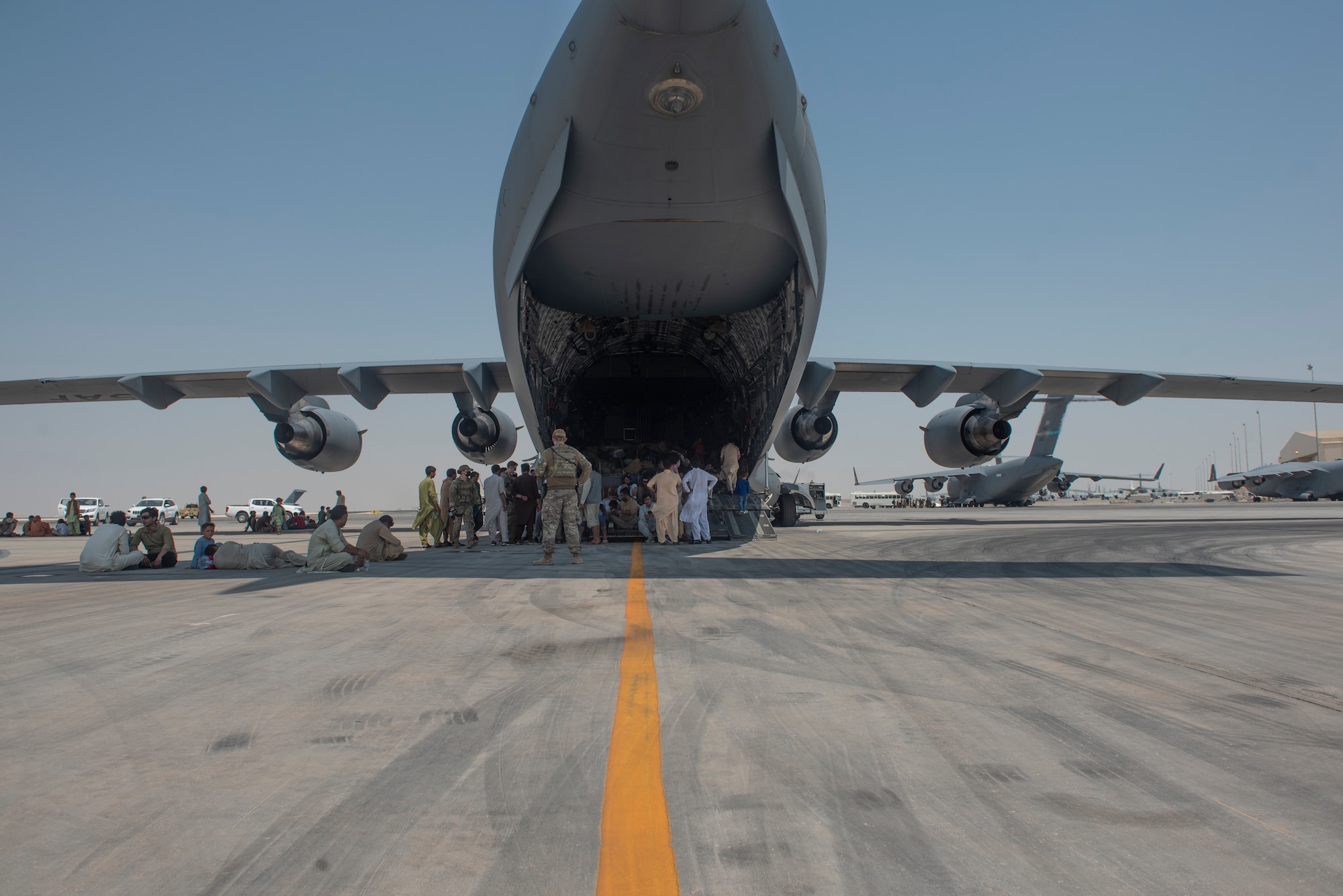 Qualified evacuees wait on the flight line as they debark a C-17 Globemaster lll Aug. 20, 2021.