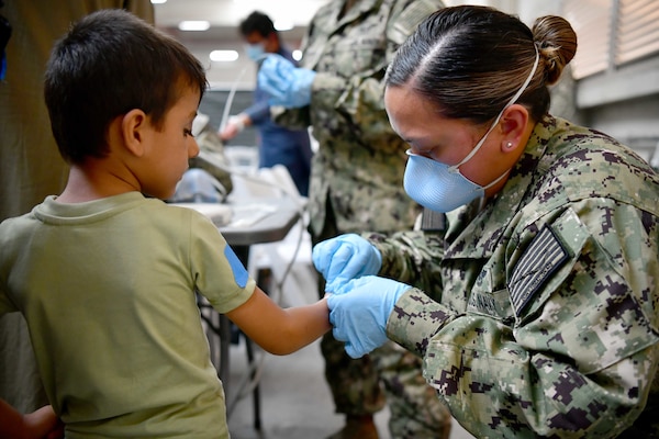 A Sailor helps an Afghan evacuee at Naval Air Station Sigonella.