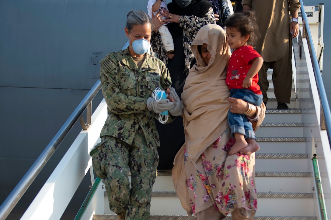 A sailor holds the hand of an evacuee holding a baby down the steps of an aircraft.