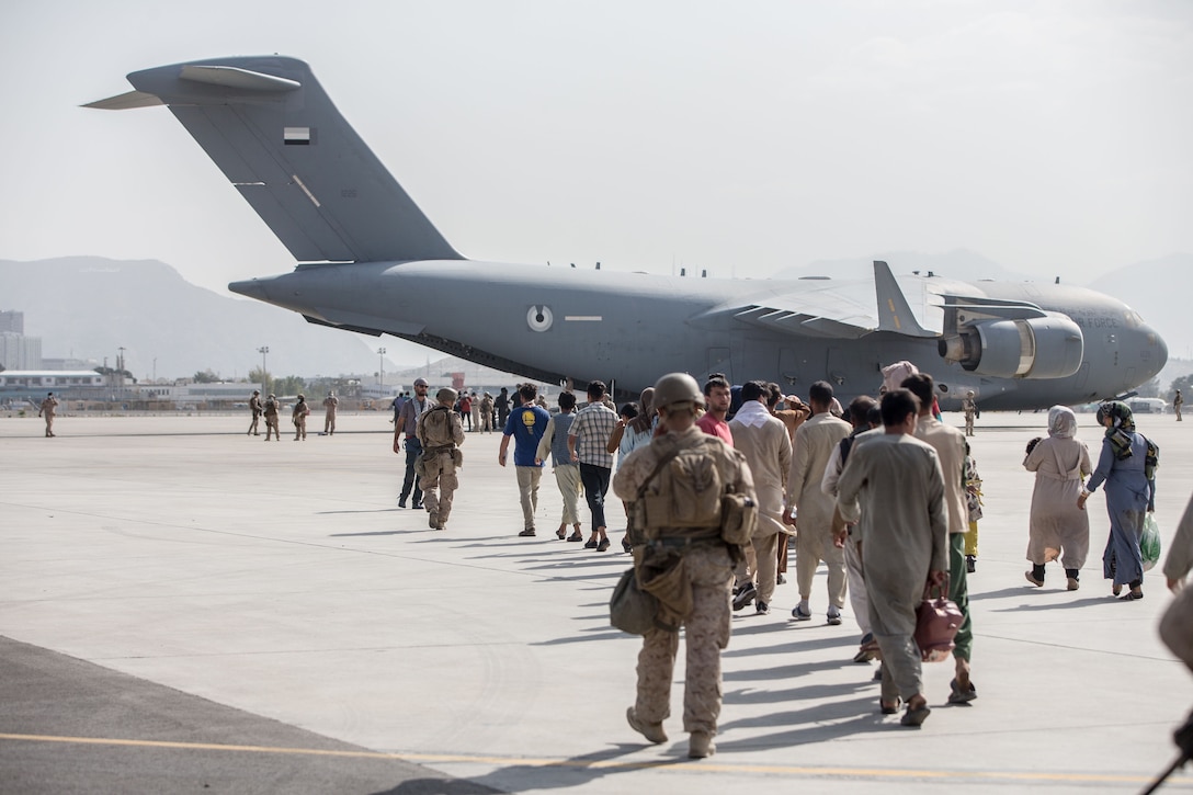 A Marine escorts a group of people walking toward an aircraft.