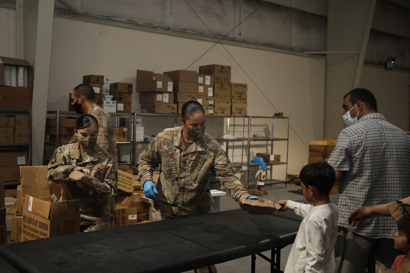 A U.S. Army Soldier passes out food to an Afghan boy. Soldiers provide meals, water, and snacks to Special Immigration Applicants seeking relocation to the United States. (U.S. Army photo by Sgt. Jimmie Baker)
