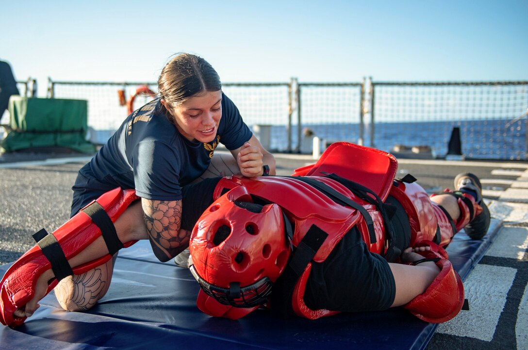 A sailor takes down a service member wearing protective gear during training on a ship.