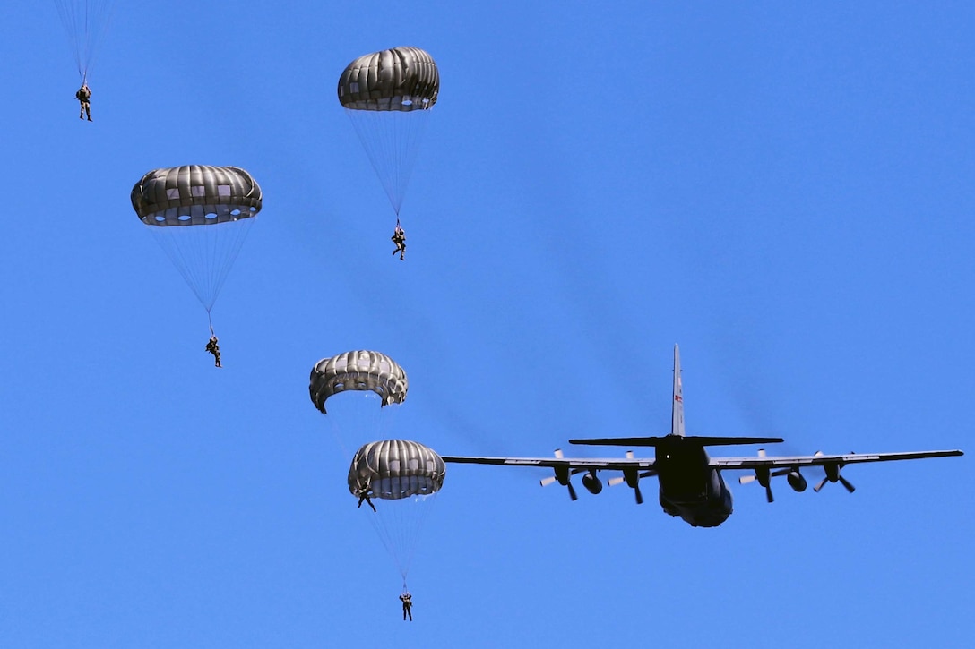 A group of soldiers parachute out of a large aircraft against a blue sky.