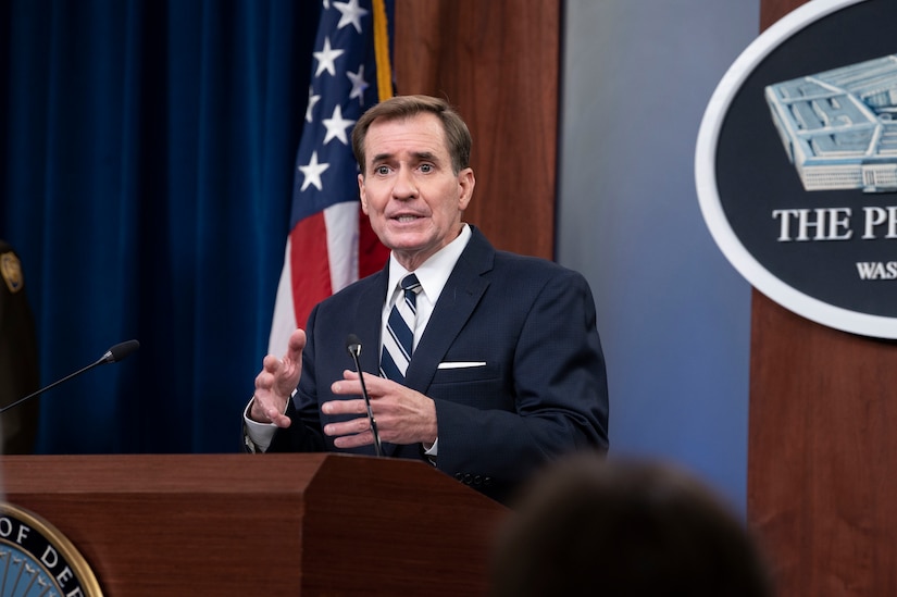 A man dressed in a business suit stands at a lectern.