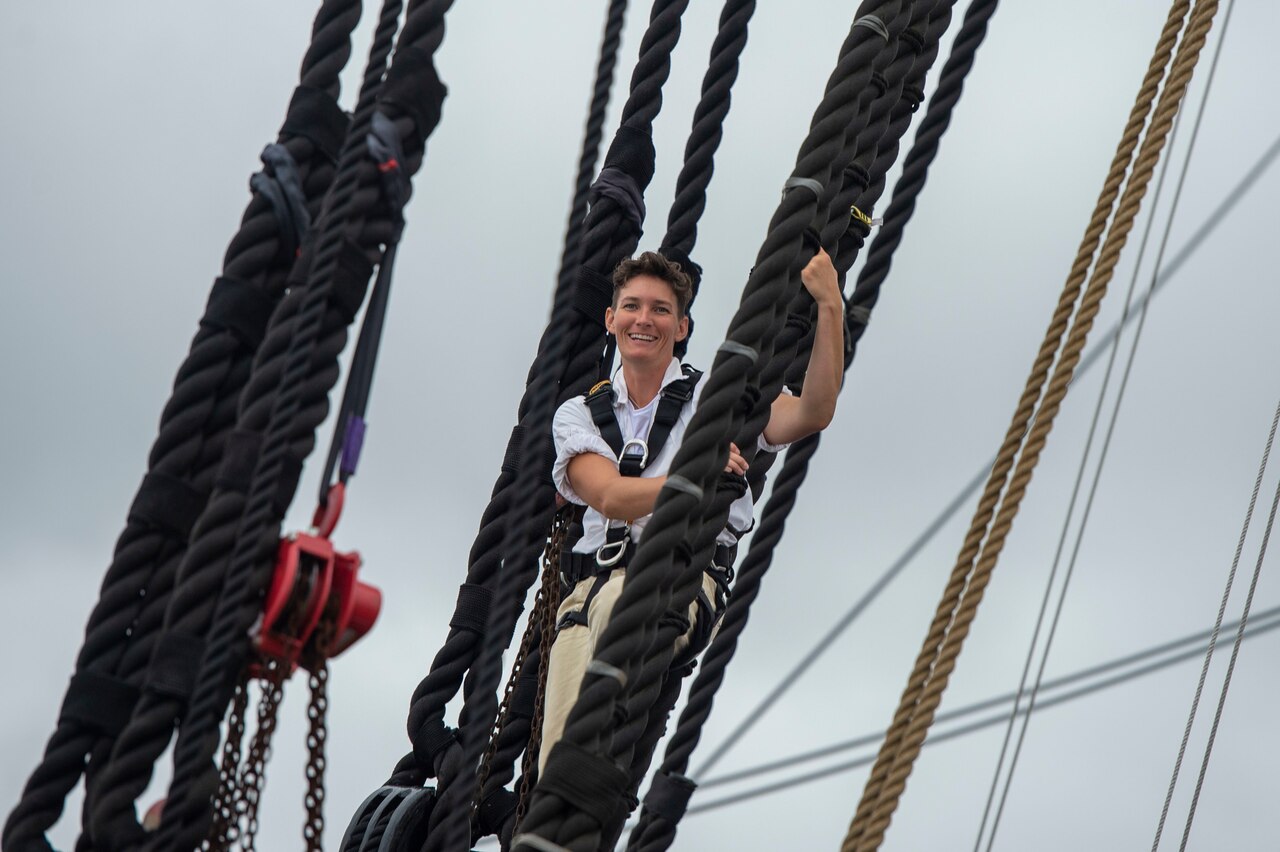 A sailor poses for a photo while holding onto lines aboard a tall ship.