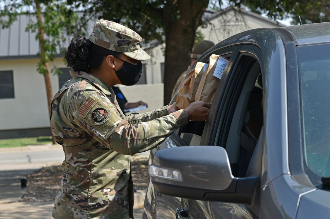 An airman hands two bags of snacks to a motorist through a car window.