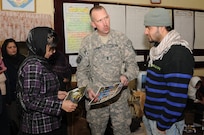 U.S. 1st Sgt. Wendell Barney, center, Bravo Battery, 1st Battalion, 101st Field Artillery Regiment (1-101st), Vermont Army National Guard, gives pictures of residents from Vermont putting together school supply donations to a teacher, left, at Ariana School on Nov. 10, 2010 in Kabul, Afghanistan. Soldiers of the 1-101st have 'adopted' the mostly girl school by providing three more classrooms and donating school supplies several times since May.