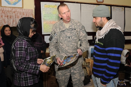 U.S. 1st Sgt. Wendell Barney, center, Bravo Battery, 1st Battalion, 101st Field Artillery Regiment (1-101st), Vermont Army National Guard, gives pictures of residents from Vermont putting together school supply donations to a teacher, left, at Ariana School on Nov. 10, 2010 in Kabul, Afghanistan. Soldiers of the 1-101st have 'adopted' the mostly girl school by providing three more classrooms and donating school supplies several times since May.