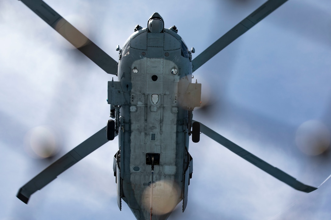 A photo shows the underside of a large military helicopter in the air.