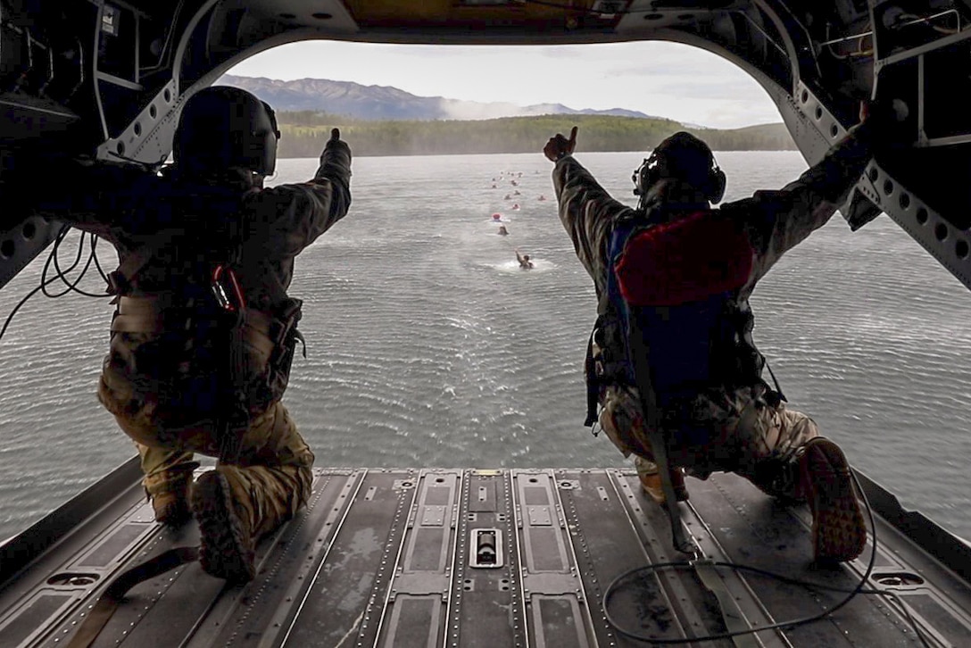 Two soldiers give the 'thumbs up' sign to a line of paratroopers in the water.