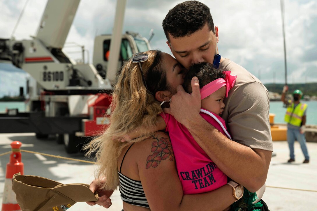 A sailor hugs his wife and daughter.