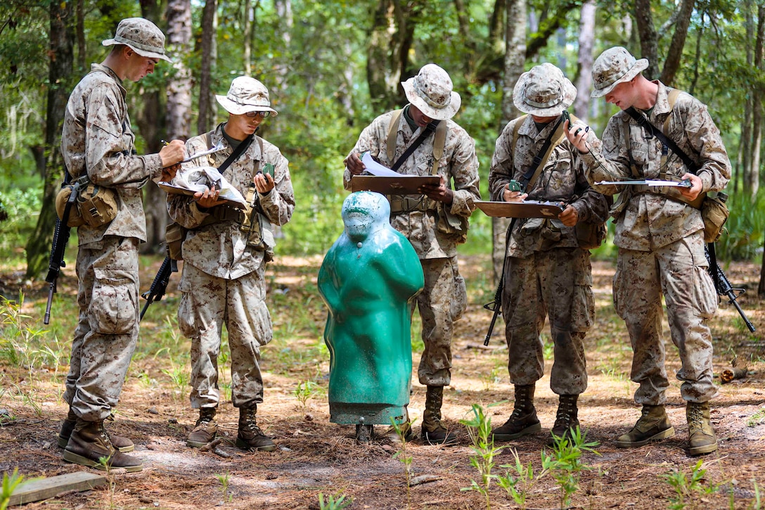 Marine Corps recruits stand in a wooded area next to a sculpture.