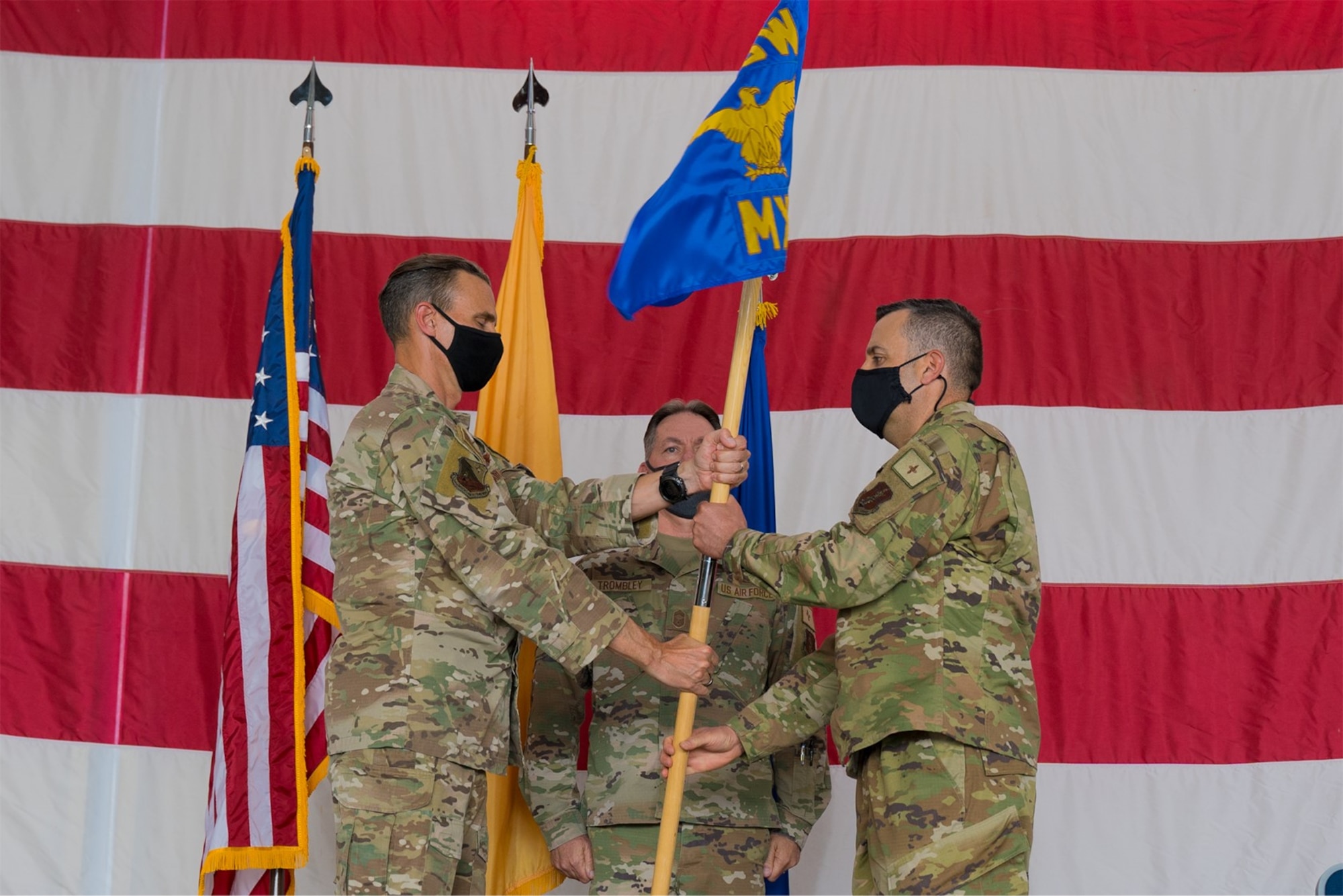 A colonel in uniform hands a command flag to a lieutenant colonel during a ceremony on a stage.
