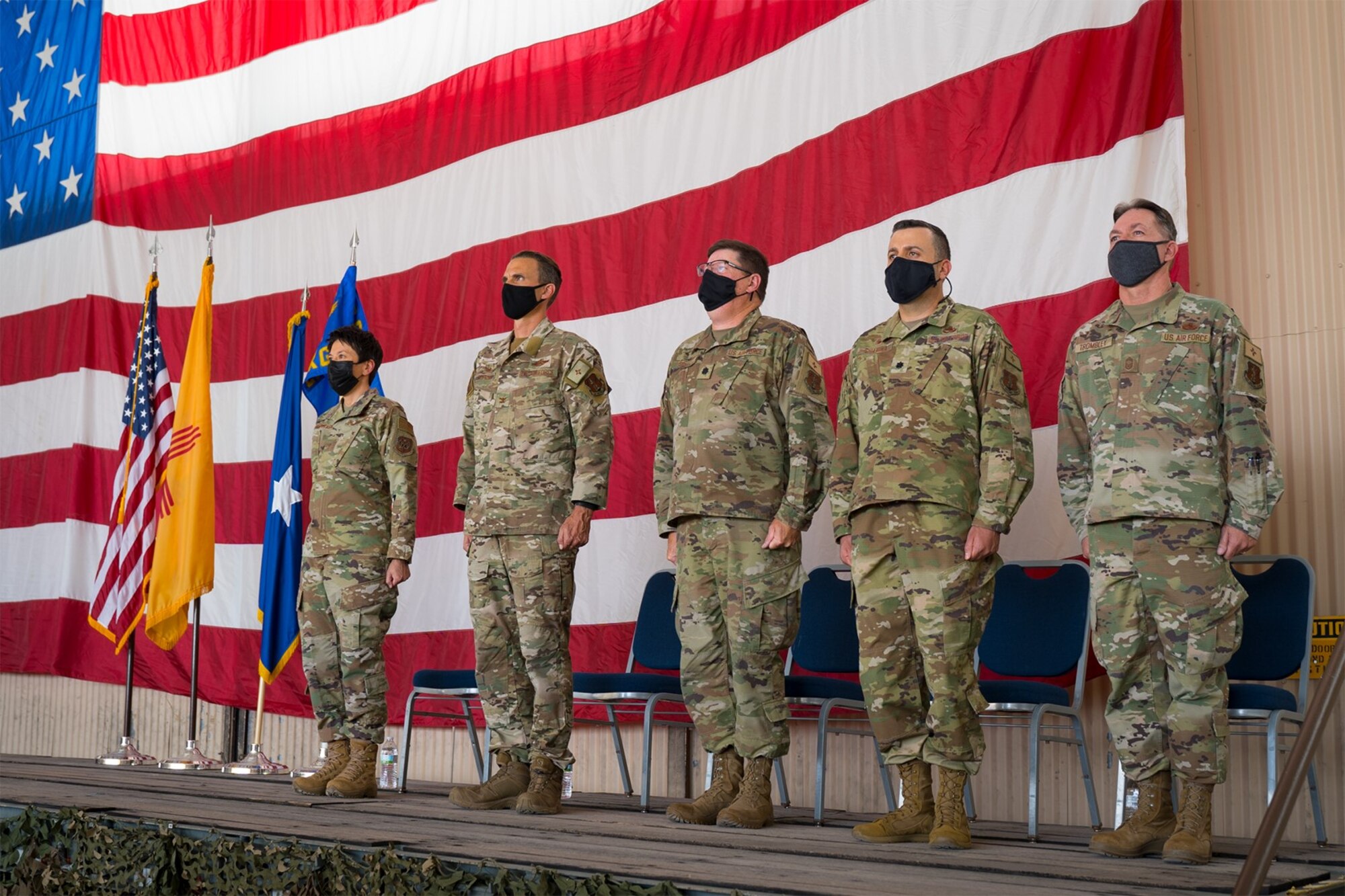 Five of the New Mexico Air National Guard senior leaders stand at attention on a stage during a ceremony.