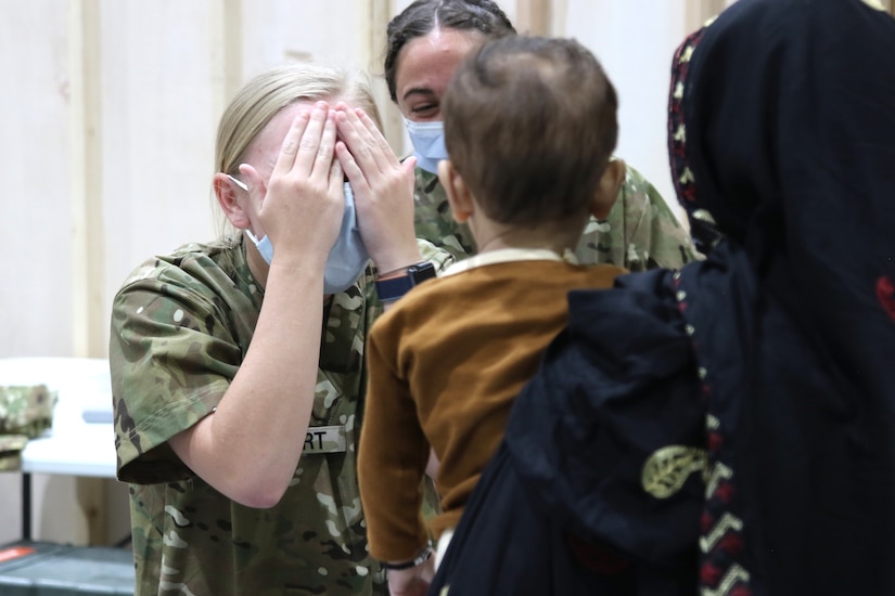 A U.S. Army National Guard Soldier with Task Force Spartan, U.S. Army Central, plays a quick game of peekaboo with an Afghan child who recently arrived at Camp Buehring, Kuwait, Aug. 23, 2021. U.S. Army Soldiers continue to work with their U.S. Central Command and Department of State teammates to support Afghanistan evacuation efforts with transportation, security, logistics and medical assistance at locations in Kuwait. (U.S. Army Photo by 1st Lt.  James Mason)