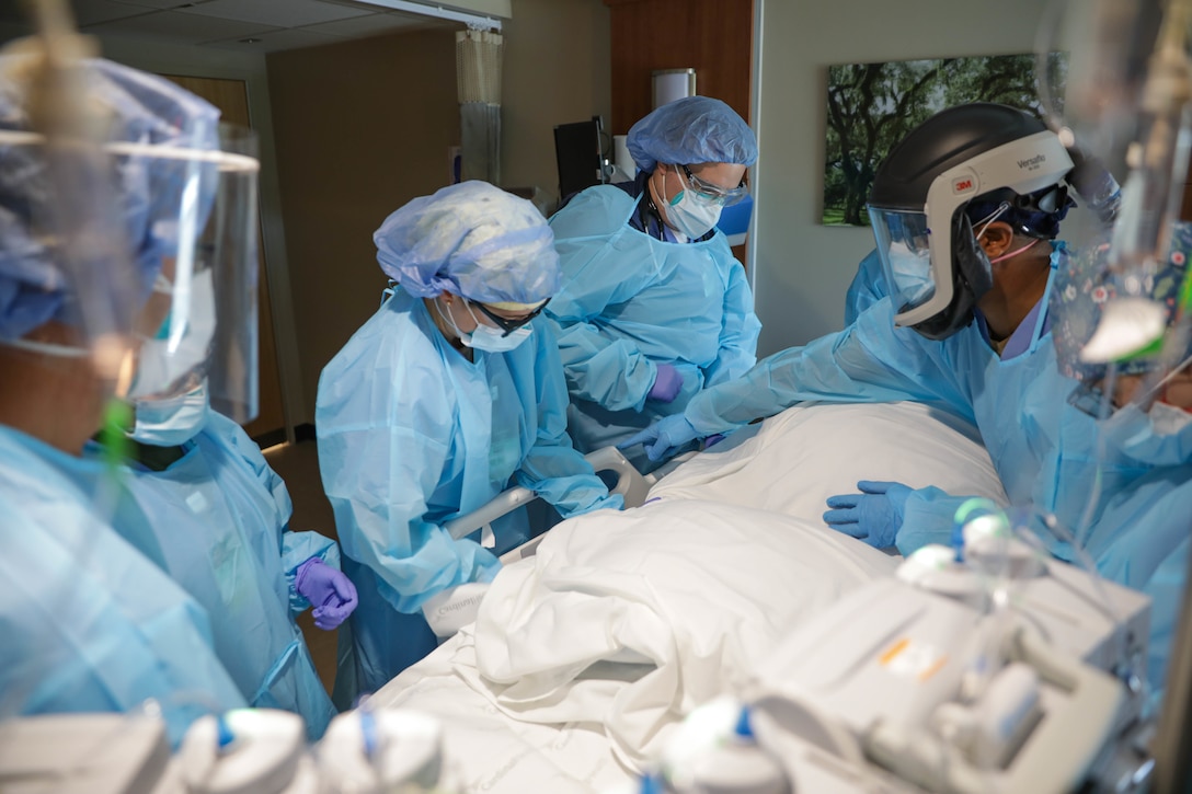 U.S. Navy. Capt. Sean McKay, a physician from Navy Medicine Readiness and Training Command Bethesda and the medical support team (MST) senior medical officer, right, directs MST members while moving a COVID positive patient to the prone position.