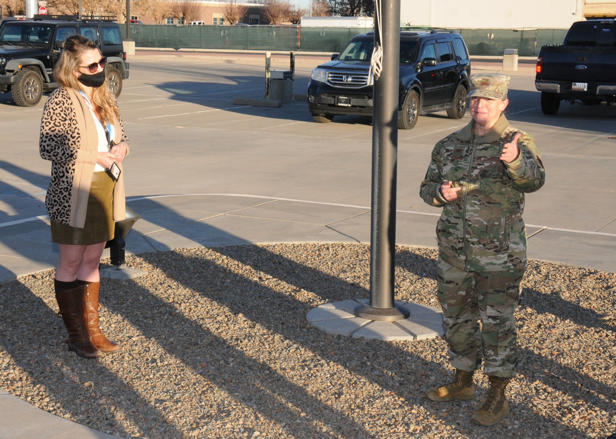 a civilian woman and an Air Force officer stand outside at the base of a flagpole.