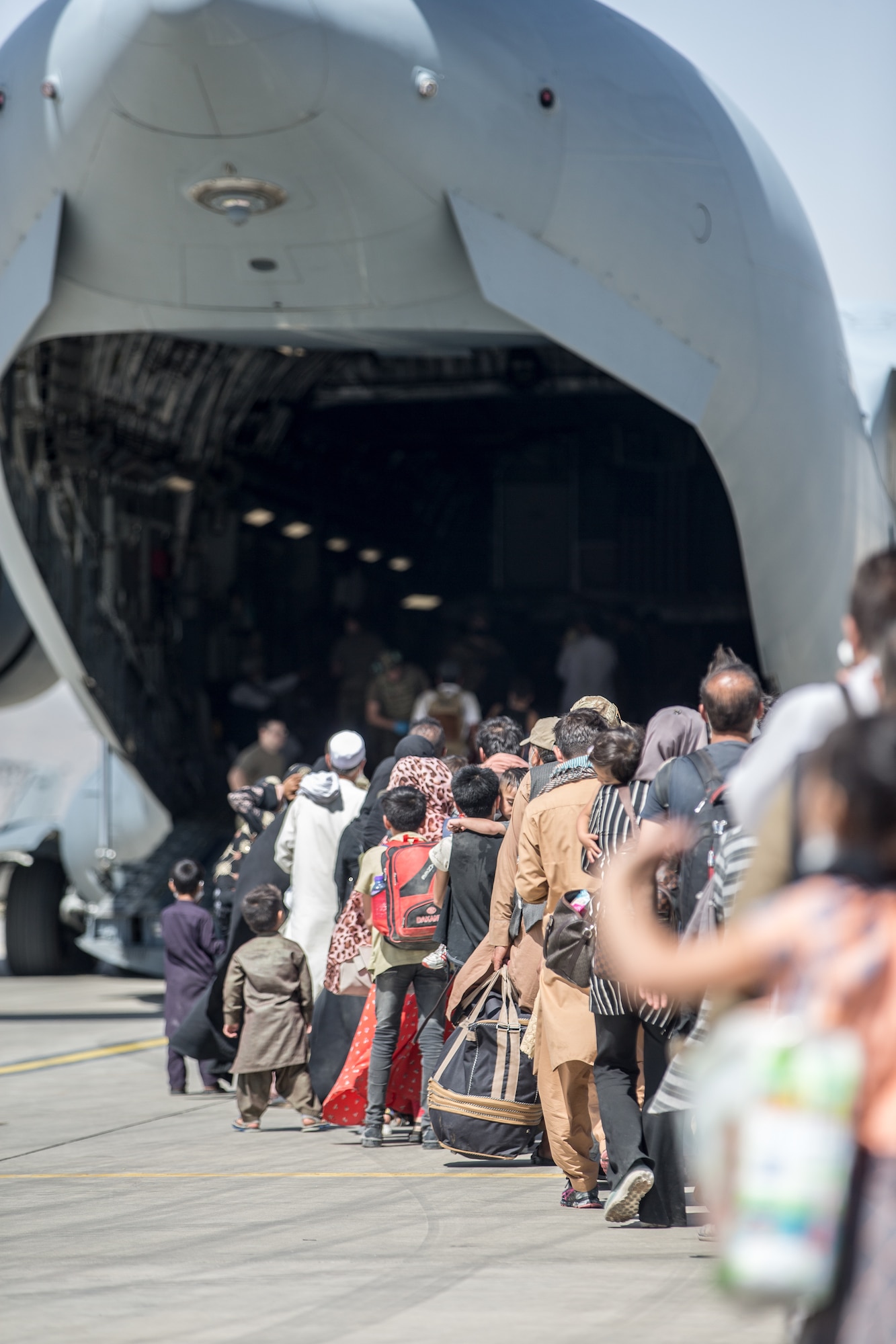 A long line of civilians enter the back of an aircraft.