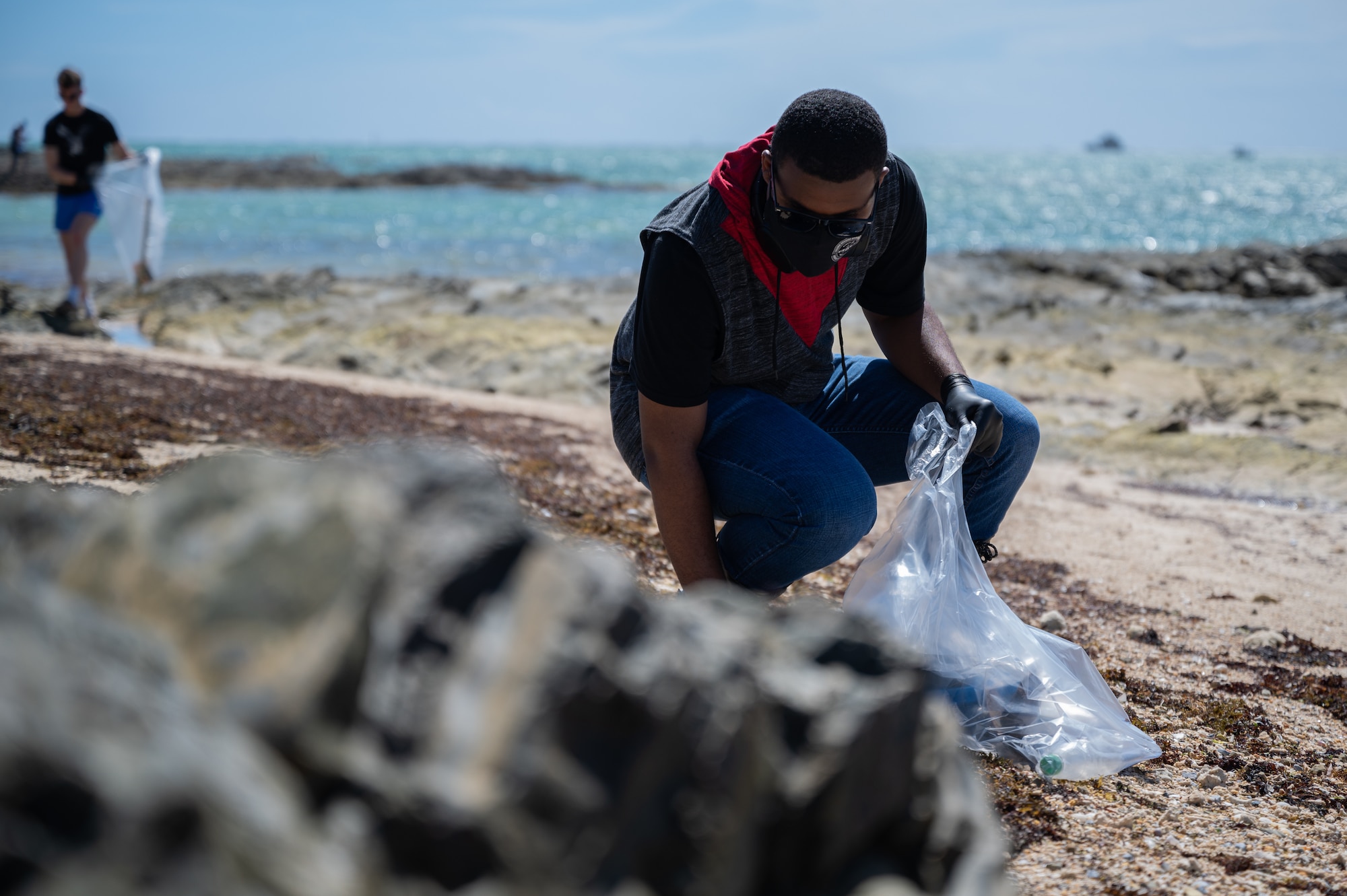 U.S. Air Force Airman Christian Johnson, 353rd Special Operations Support Squadron electrical environmental apprentice, picks up garbage at Seaglass Beach on Okinawa, Japan, Aug. 21, 2021. Beach clean-ups not only benefit the local wildlife, but can also help ecosystems globally since trash can be carried by the ocean. (U.S. Air Force photo by Airman 1st Class Stephen Pulter)