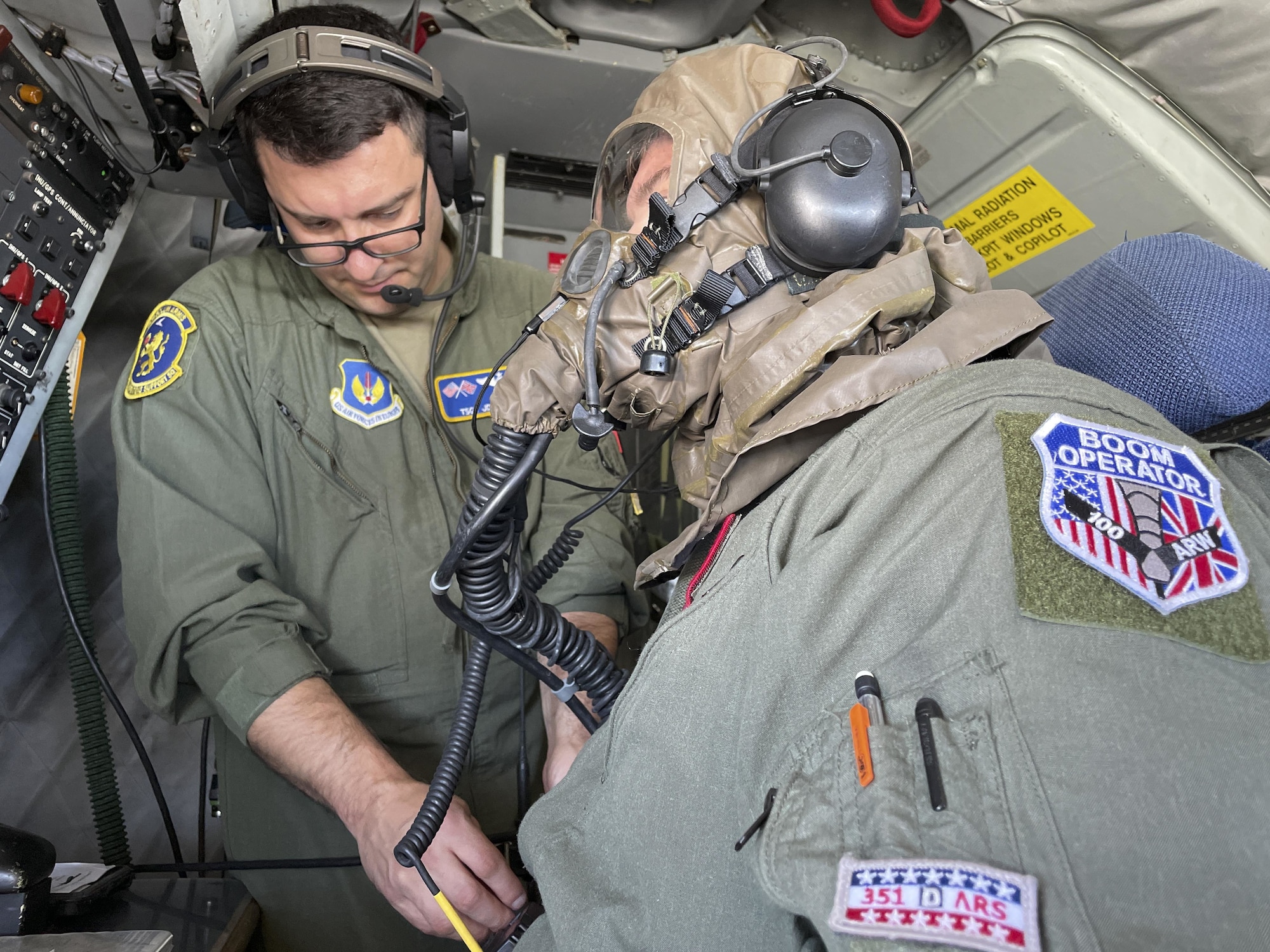 U.S. Air Force Tech. Sgt. Juan Upegui, 351st Air Refueling Squadron boom operator, left, assists Airman 1st Class Daniel Crump, 351st ARS boom operator, with donning his gas mask to meet a training requirement during a refueling mission over Europe Aug. 19, 2021. The 100th Air Refueling Wing is the only permanent U.S. air refueling wing in the European theater, providing the critical air refueling “bridge” which allows the expeditionary Air Force to deploy around the globe at a moment’s notice. (U.S. Air Force photo by Senior Airman Joseph Barron)