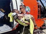 A Coast Guard air crew member helps transport a critically injured child from the helicopter to awaiting emergency medical services at Port au Prince, Haiti, Aug. 15, 2021. U.S. Coast Guard forward deployed Jayhawk helicopter crews are from Air Station Clearwater, Florida. (U.S. Coast Guard photo by Lt. David Steele)