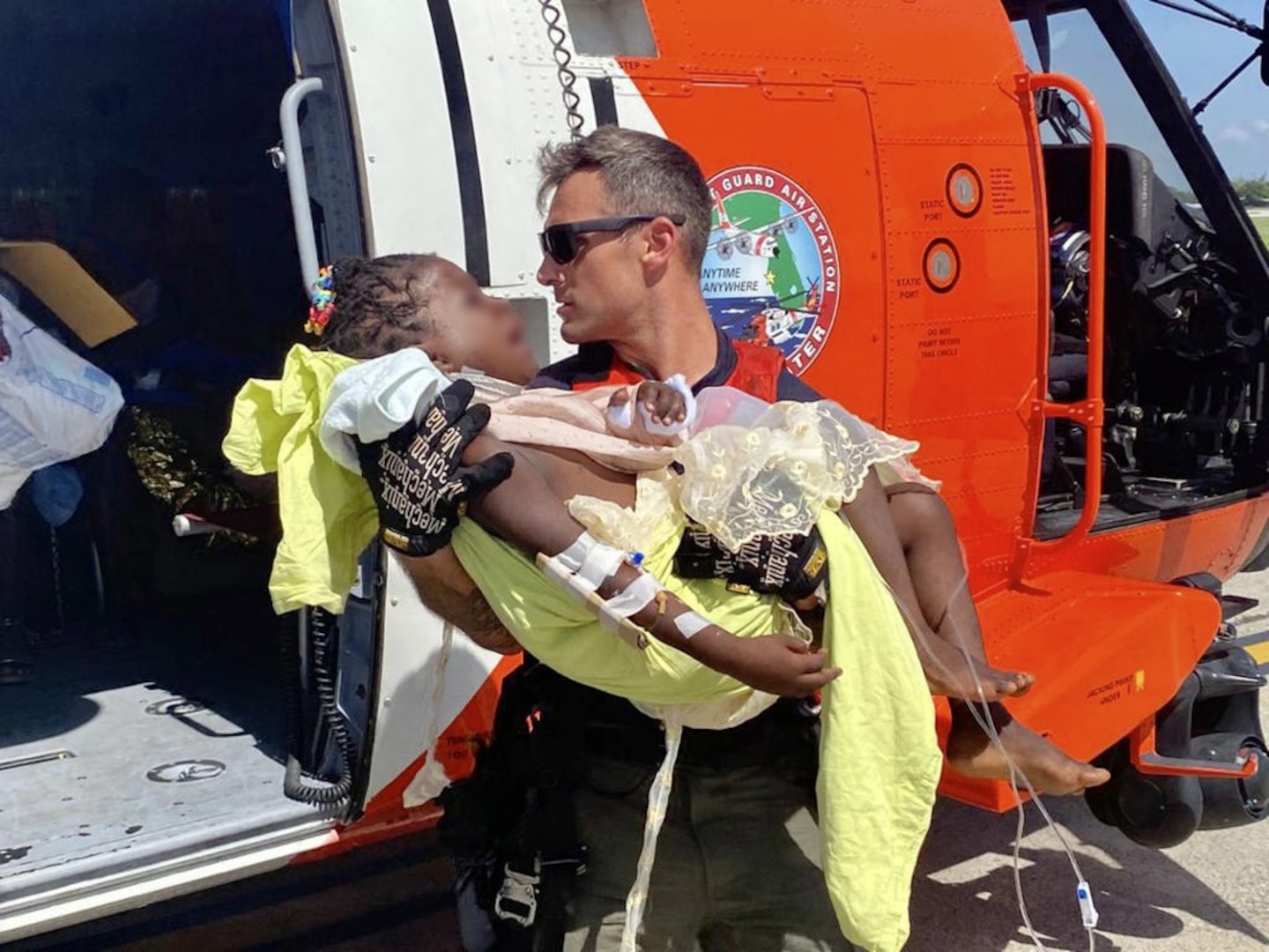 A Coast Guard air crew member helps transport a critically injured child from the helicopter to awaiting emergency medical services at Port au Prince, Haiti, Aug. 15, 2021. U.S. Coast Guard forward deployed Jayhawk helicopter crews are from Air Station Clearwater, Florida. (U.S. Coast Guard photo by Lt. David Steele)