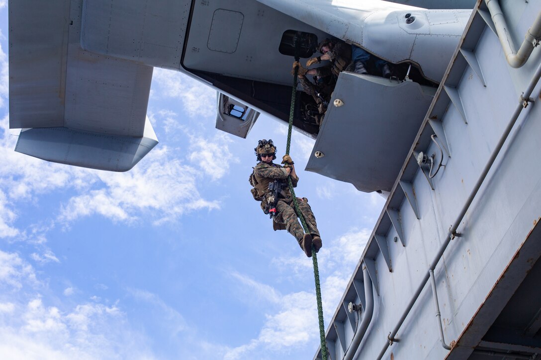 A Marine holds onto a rope dangling from an aircraft.