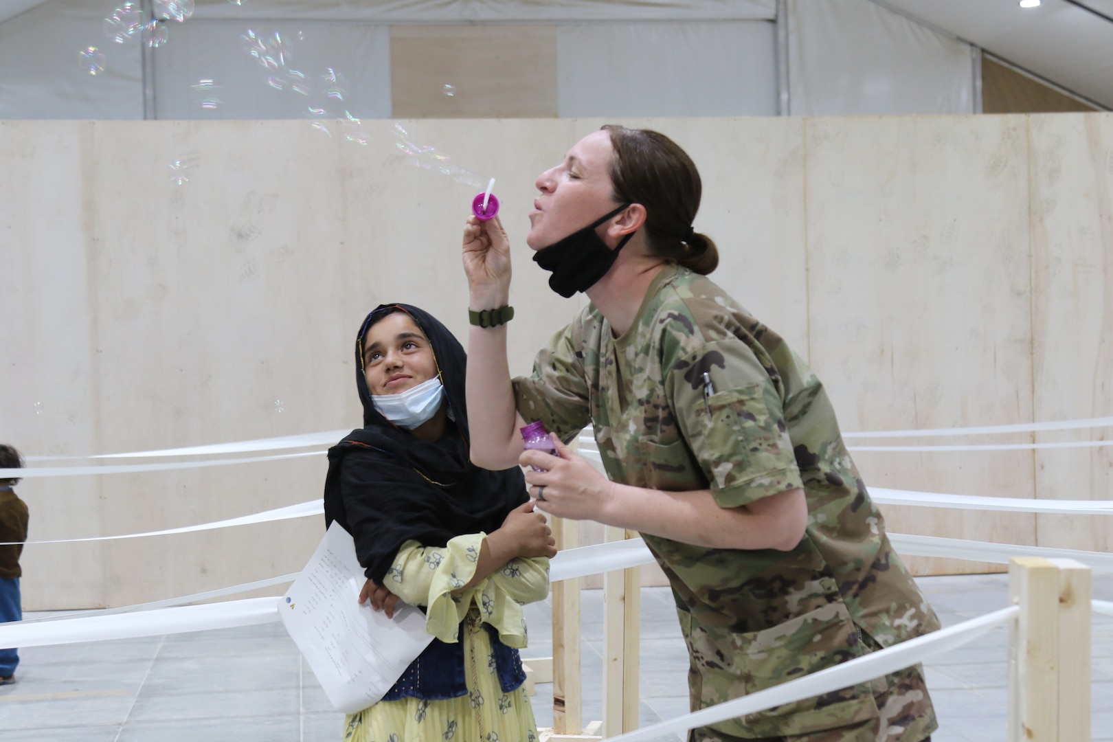A U.S. Army National Guard Soldier with Task Force Spartan, U.S. Army Central, entertains an Afghan girl with bubbles as she waits to in-process at Camp Buehring, Kuwait, Aug. 23, 2021.