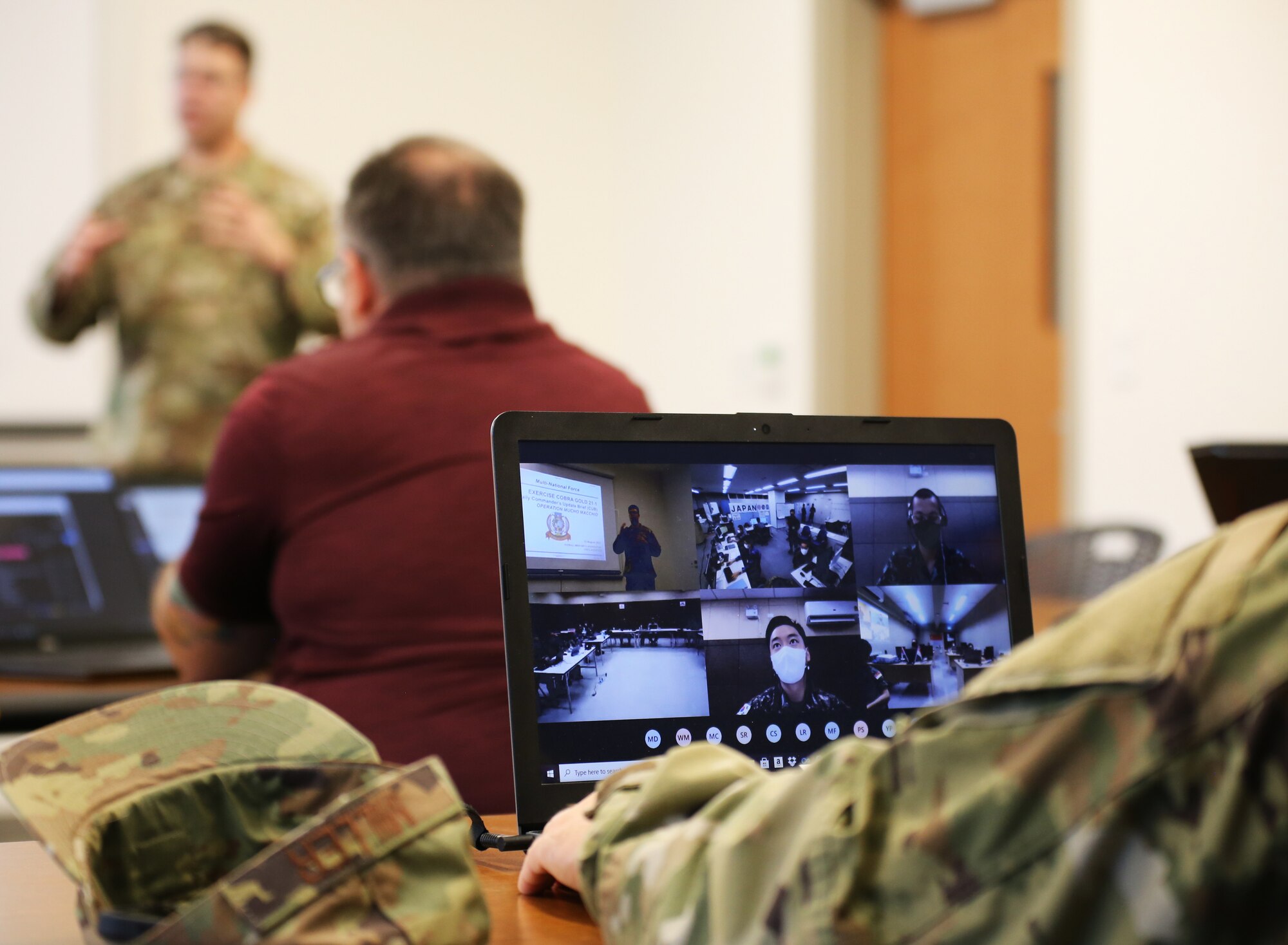 In the background Lt. Col. Jason Silves, 194th Wing, Washington Air National Guard conducts a briefing via Teams with partners in four different countries during Cobra Gold 21 Cyber Exercise at Camp Murray, Washington on August 11, 2021. (U.S. National Guard photo by Joseph Siemandel)